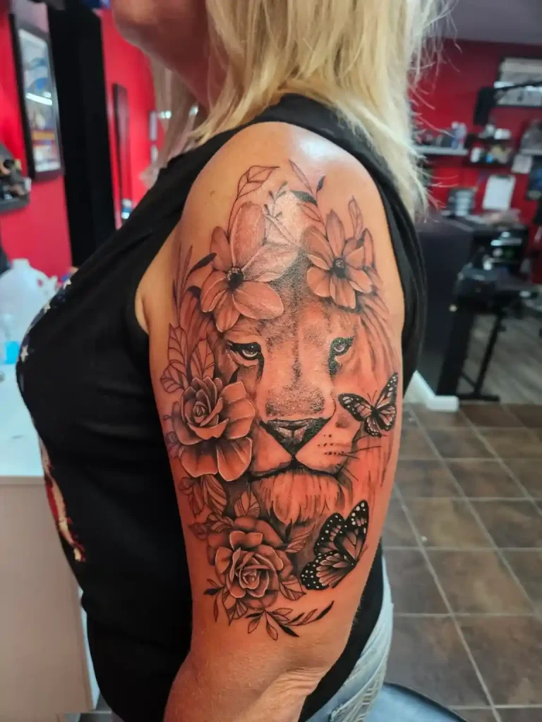 Fine line lion tattoo on shoulder with flowers and butterflies, black and grey
