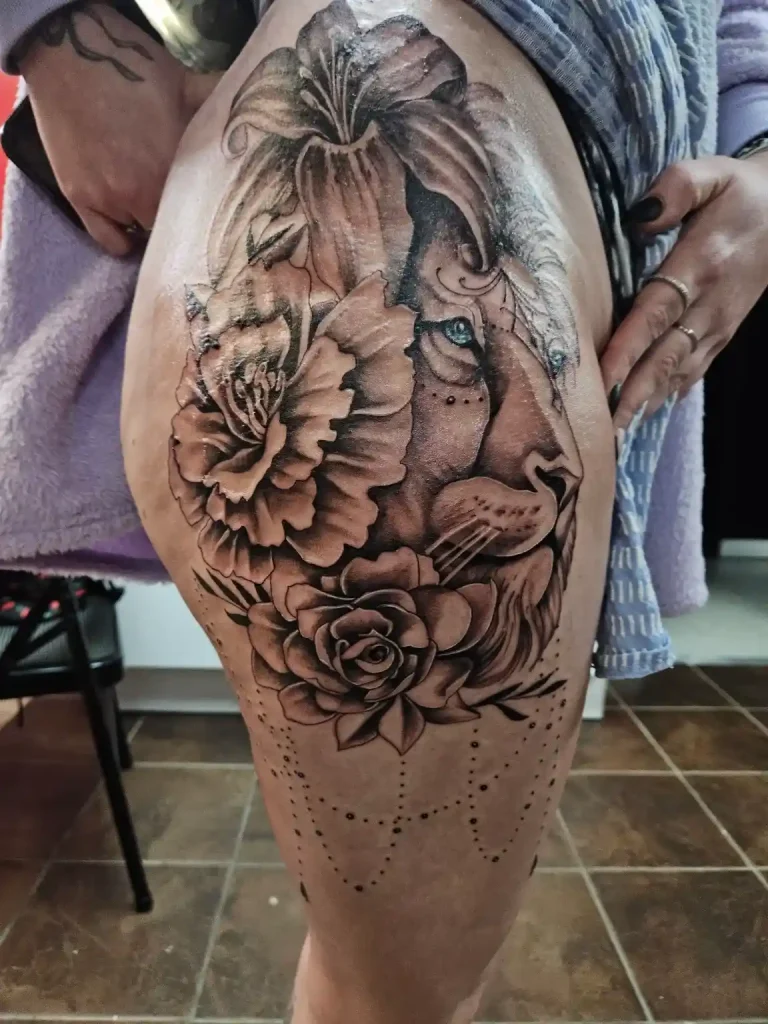 Fine line lion tattoo on thigh surrounded by roses and lily detail work