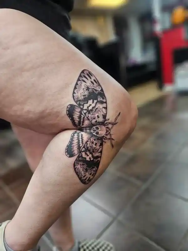 Fine line moth tattoo on thigh with detailed wing patterns, black and grey