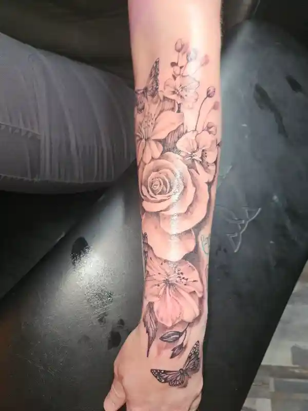 Fine line floral tattoo on forearm with roses, blossoms, and butterflies
