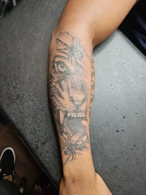 Black and grey tattoo on forearm of a tiger face with two spiders and numbered dice markings