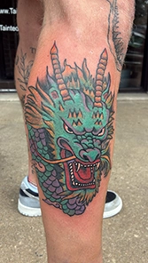 Traditional Japanese-style green dragon head tattoo on calf with purple scales, gold horns and bold red open mouth detail