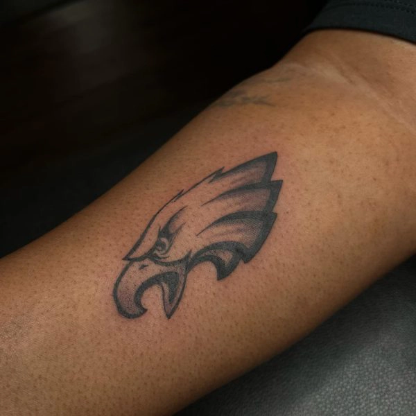Black and grey stylized eagle head tattoo on the forearm
