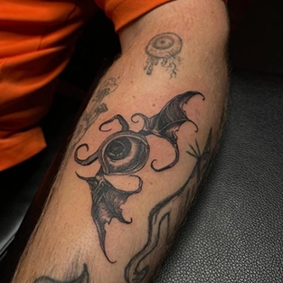 Black linework eye and bat wings tattoo on the forearm
