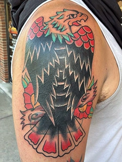 Traditional style eagle and flowers tattoo in color on the upper arm