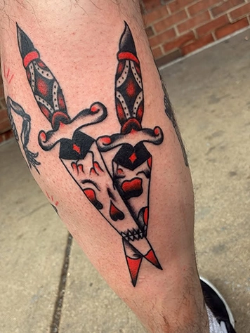 Traditional style dagger and skull tattoo in red and black on the calf