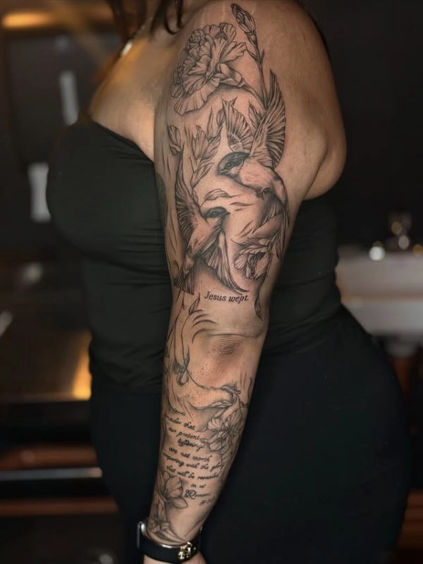 Black and grey floral and bird sleeve tattoo with script text reading Jesus wept