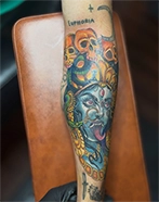 Color demon face tattoo with lettering on the lower leg