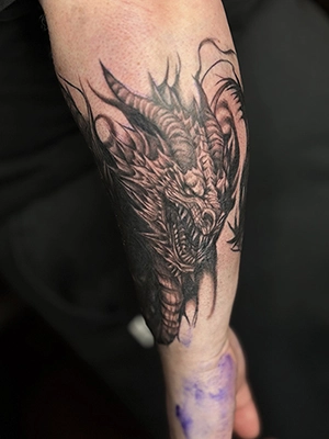 Black and grey dragon head tattoo on the forearm