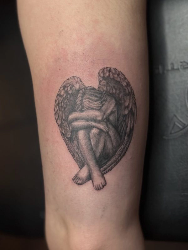 Black and grey heart shaped tattoo of an angel with wings on the forearm